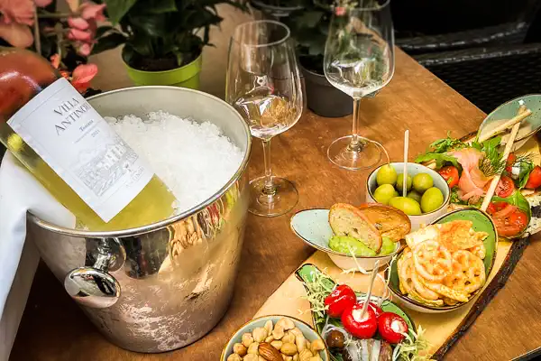 Weißwein im Weinkühler und eine Holzplatte mit italienischen Antipasti