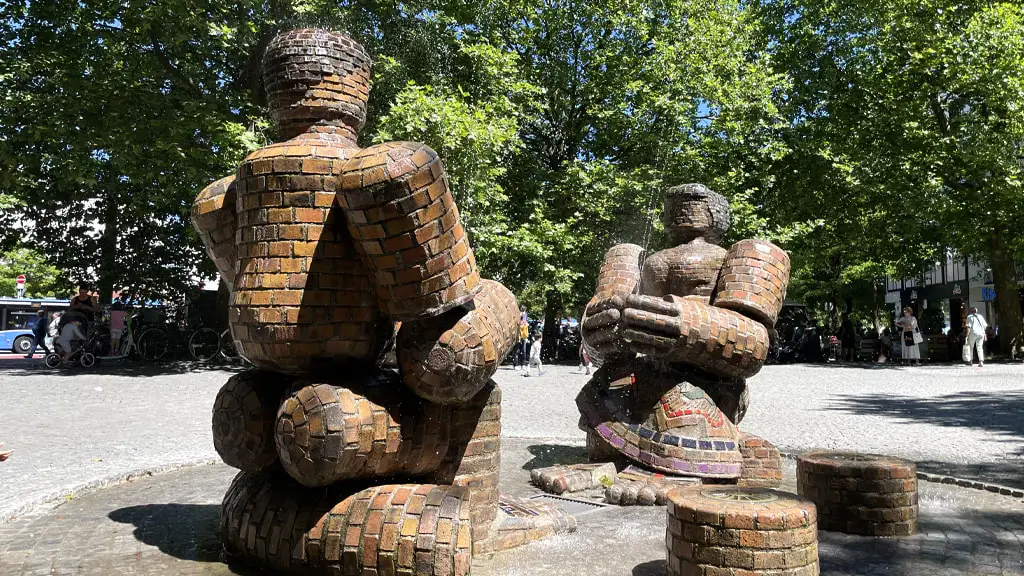 Zwei massive Figuren aus Backsteinen sitzen sich gegenüber und bilden den Brunnen steinernes Paar