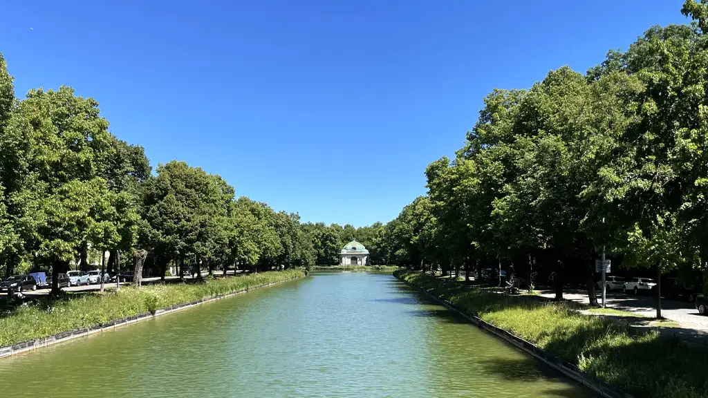 Zentralperspektivischer Blick entlang des Schlosskanals Richtung Norden mit Baumreihen auf beiden Seiten. Am Ende des Kanals sieht man den Hubertusbrunnen in Form eines kleinen Tempels.