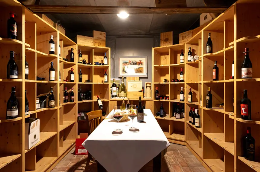 Weinkeller: Tisch mit weißer Tischdecke und zwei Weingläsern vor einem großen Weinregal in U-Form.