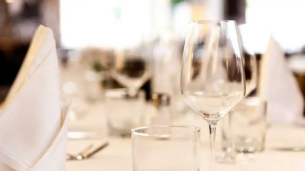 Nahaufnahme von gefalteter Serviette, Wasserglas und Weinglas: Hintergrund unscharf