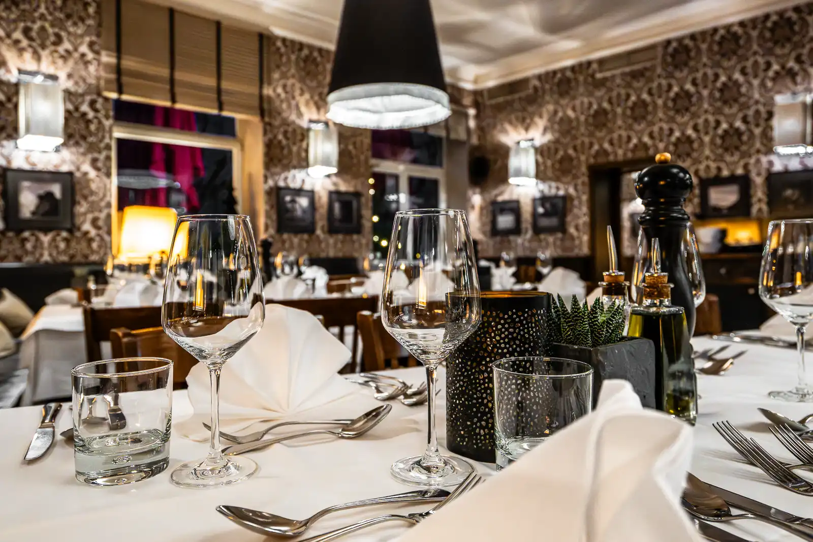 Festlich gedeckter Restaurantbereich mit weissen Tischdecken, gefalteten Servietten, Wasserflaschen, Holztischen und warmem Licht