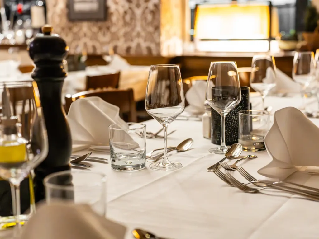 Festlich gedeckter Tisch im Ristorante ROMANS mit weissen Tischdecken, gefalteten Servietten, Weingläsern, Besteck und warmem Licht für Feiern.