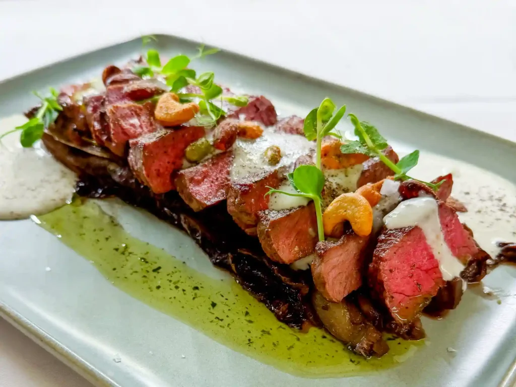 Tagliata di manzo mit in Scheiben geschnittenem, rosa Rindfleisch auf einem rechteckigen Teller.