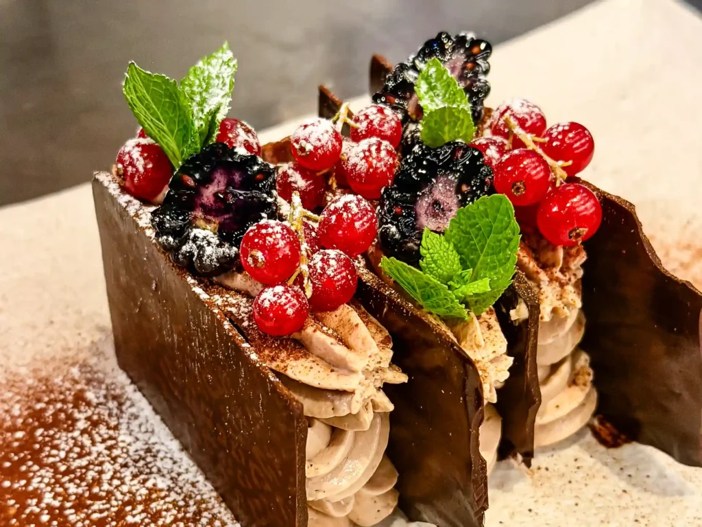 Schokoladendessert mit Creme, roten Johannisbeeren, Brombeeren, Minzblättern und Puderzucker.
